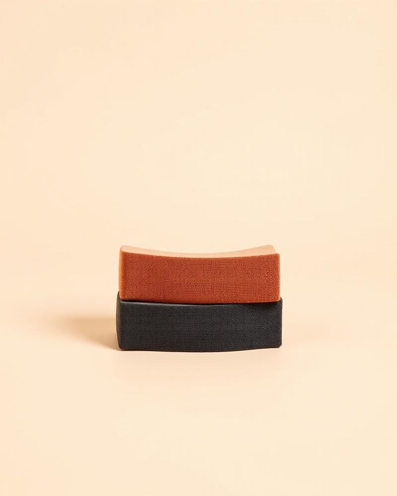Three stacked fabric resistance bands in sand, clay and charcoal on a plain neutral background