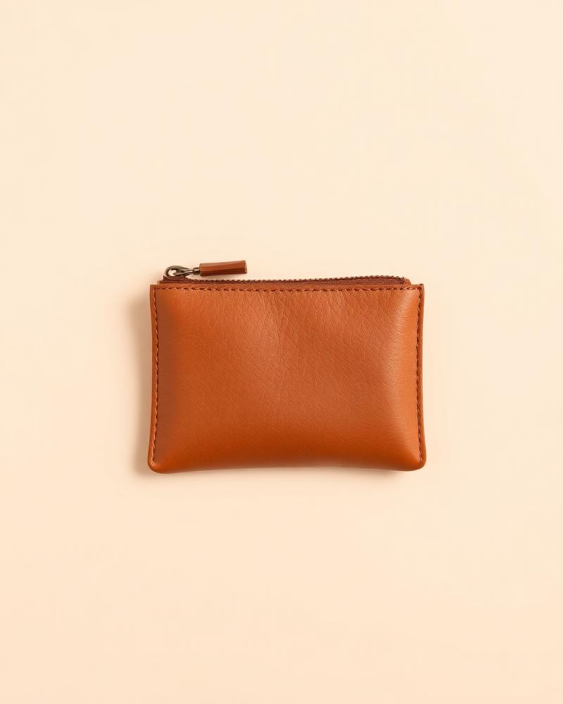 Small tan leather zip coin pouch lying flat on a plain neutral background