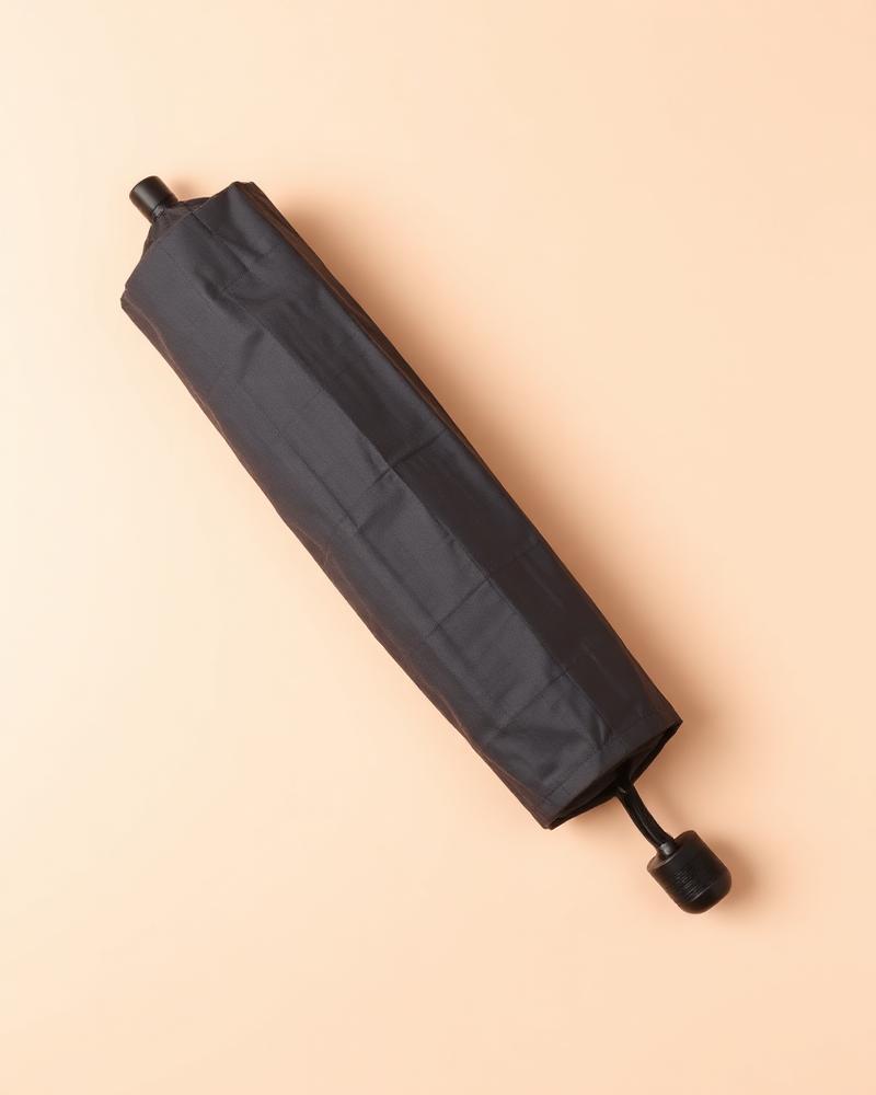 Folded charcoal compact travel umbrella photographed on a plain neutral background